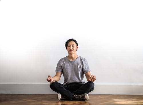 Photo of Man in Gray T-shirt and Black Jeans on Sitting on Wooden Floor Meditating