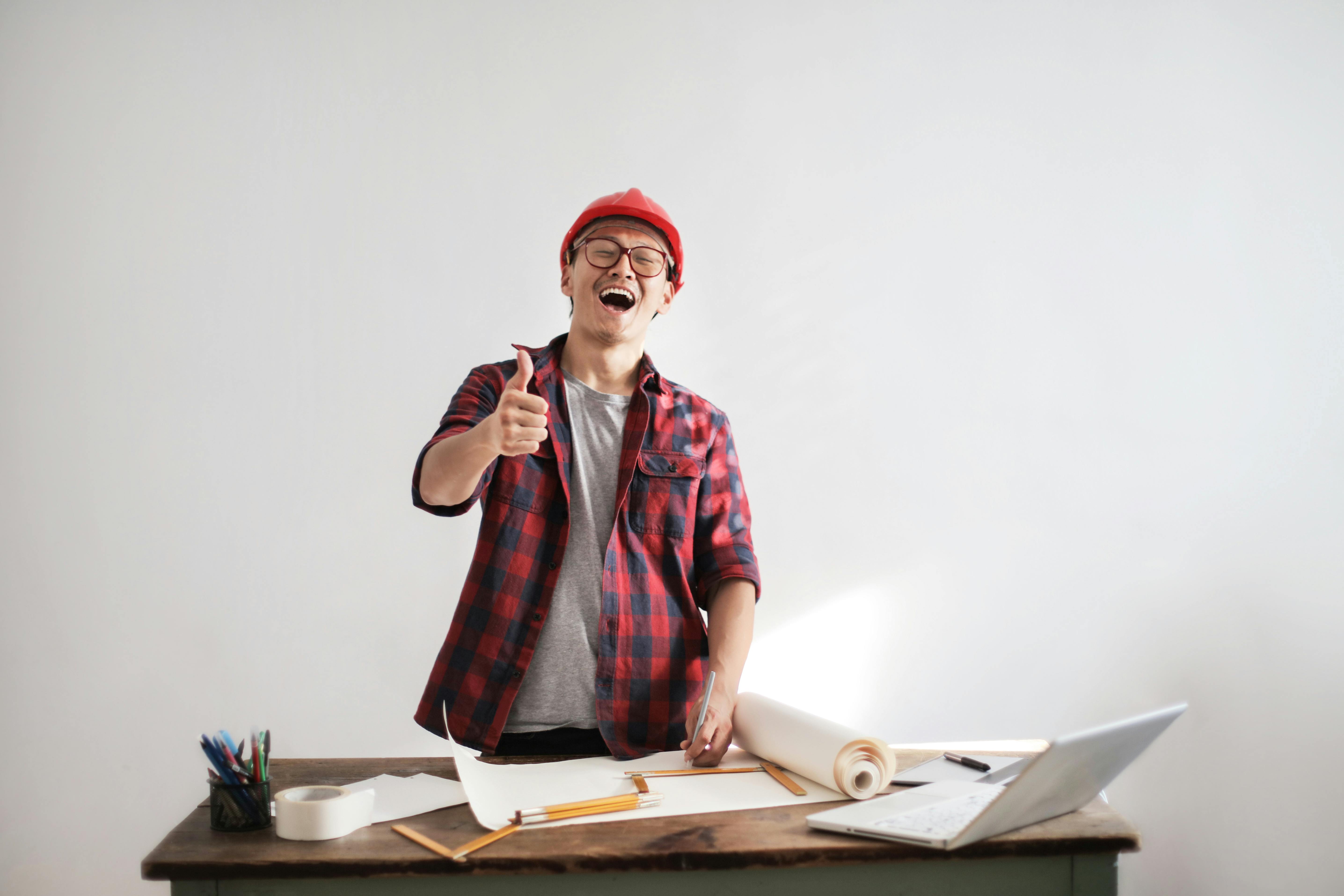 laughing male constructor showing thumb up at working desk