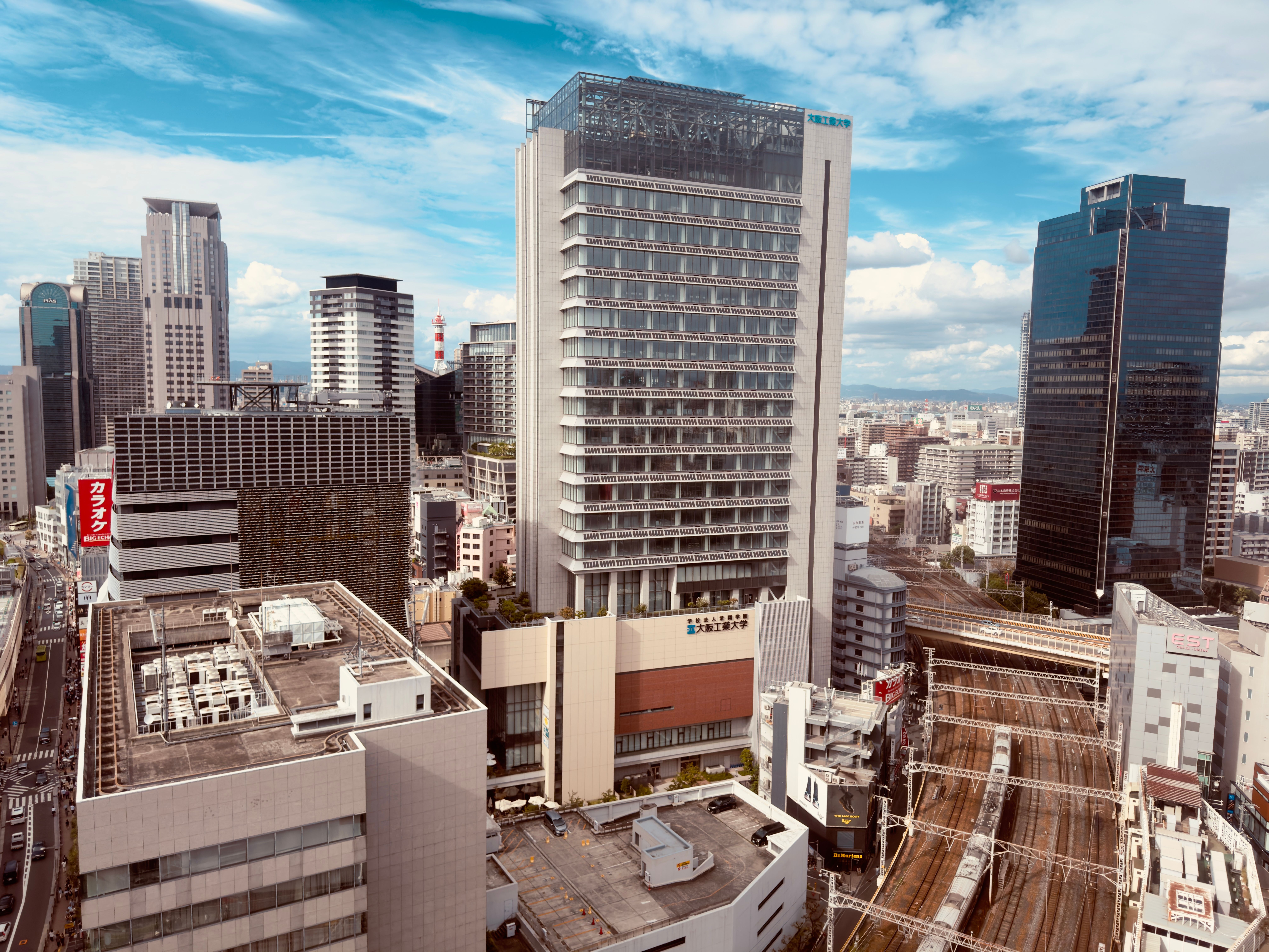 A stunning view of Osaka's cityscape featuring modern skyscrapers, high-rise buildings, and a railway on a sunny day.