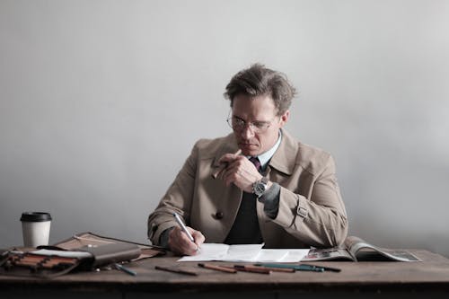 Фотография рабочего человека в коричневом пальто, сидящего за столом и курящего сигару