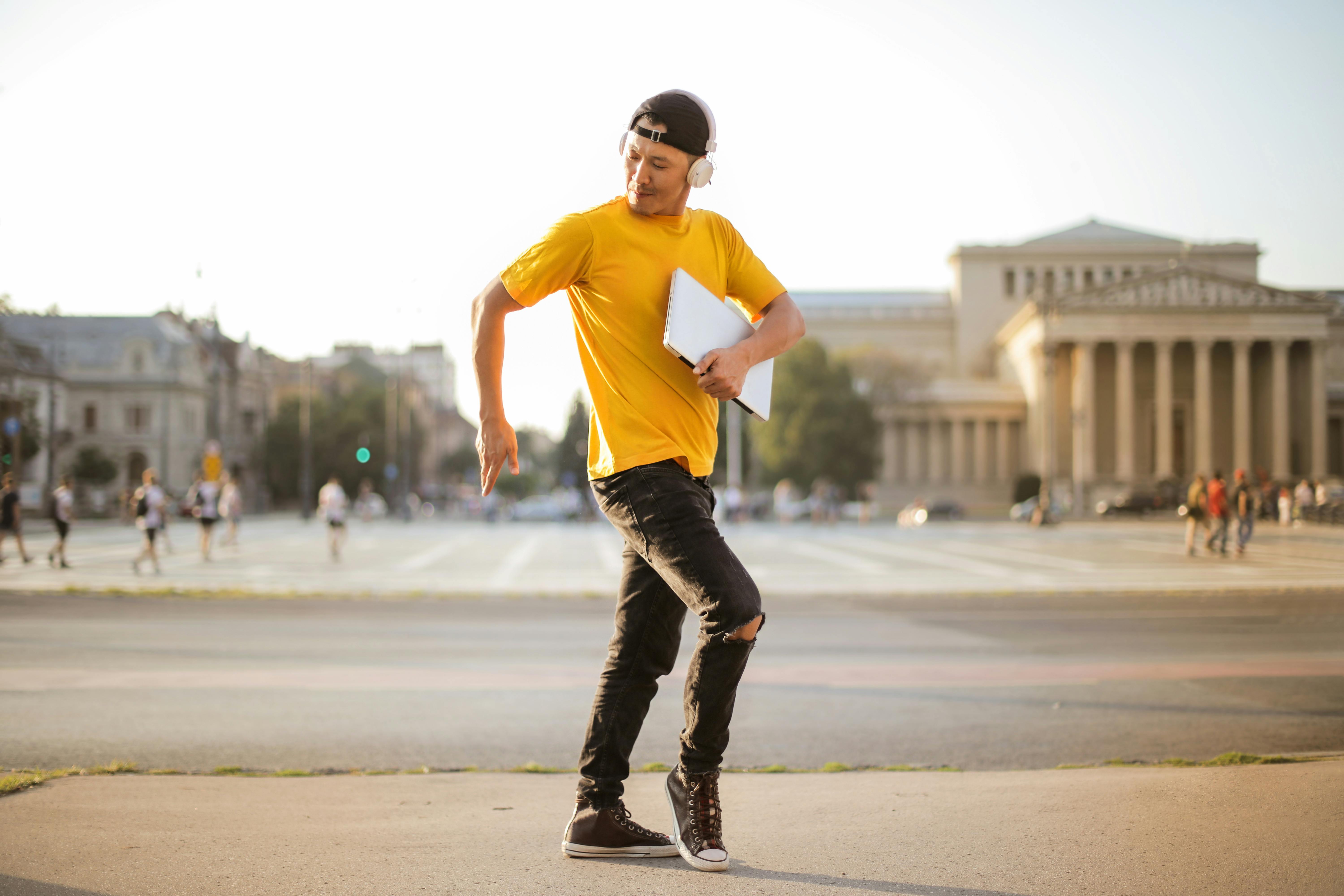 一个年轻人在户外拿着笔记本电脑，充满活力地随着音乐跳舞