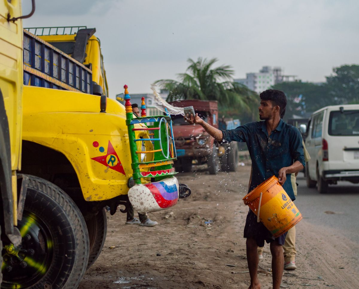 Worker hand-washing a lorry body with a bucket of water at the roadside — the safest cleaning method for lorry stickers