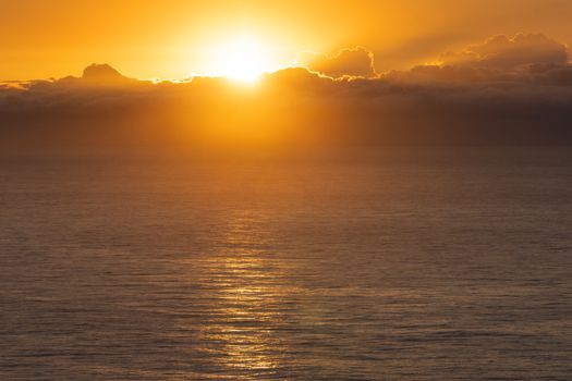Stunning sunrise over the ocean with golden clouds and reflections on water.