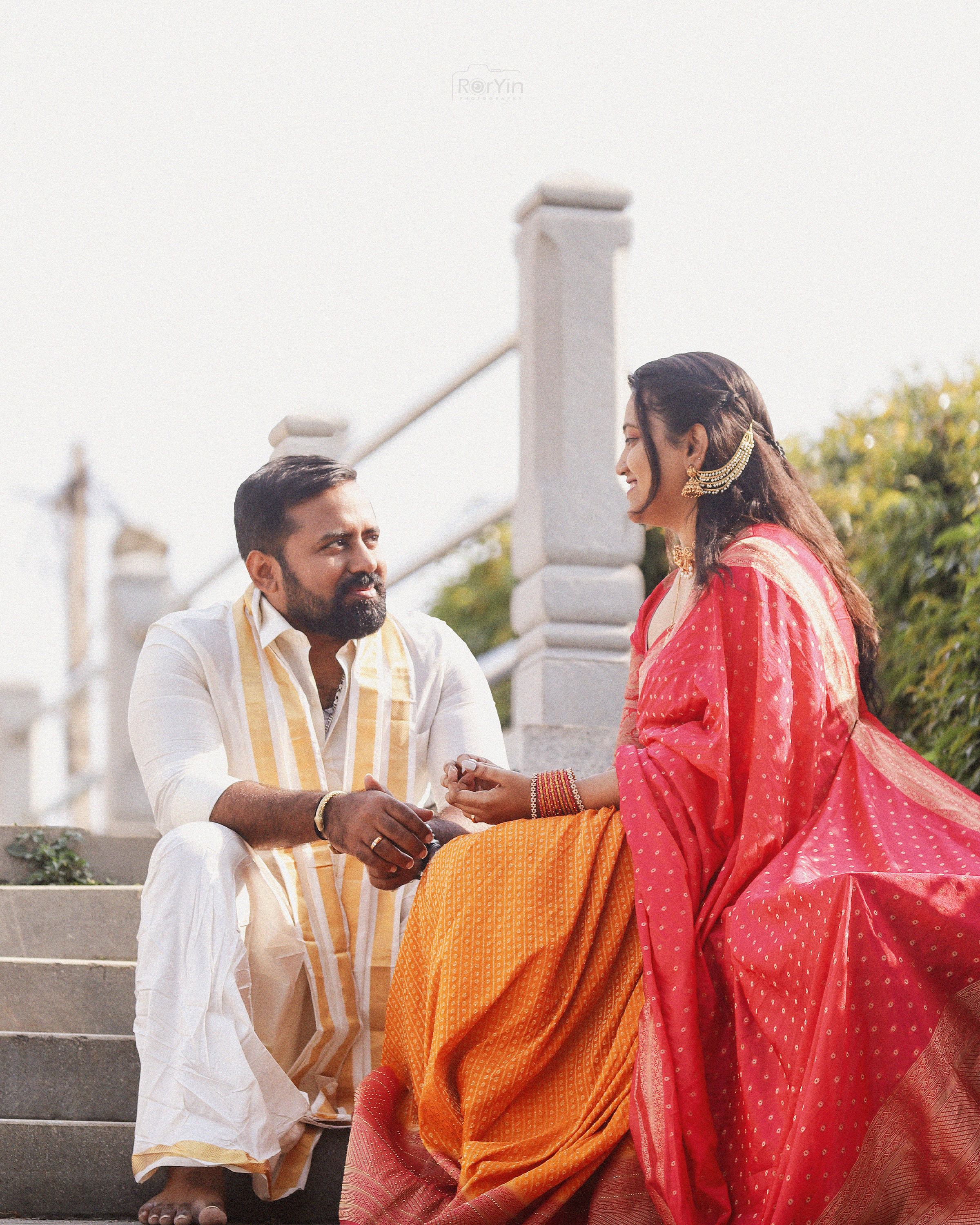 Couple in traditional attire enjoying a candid moment on stone steps outdoors.