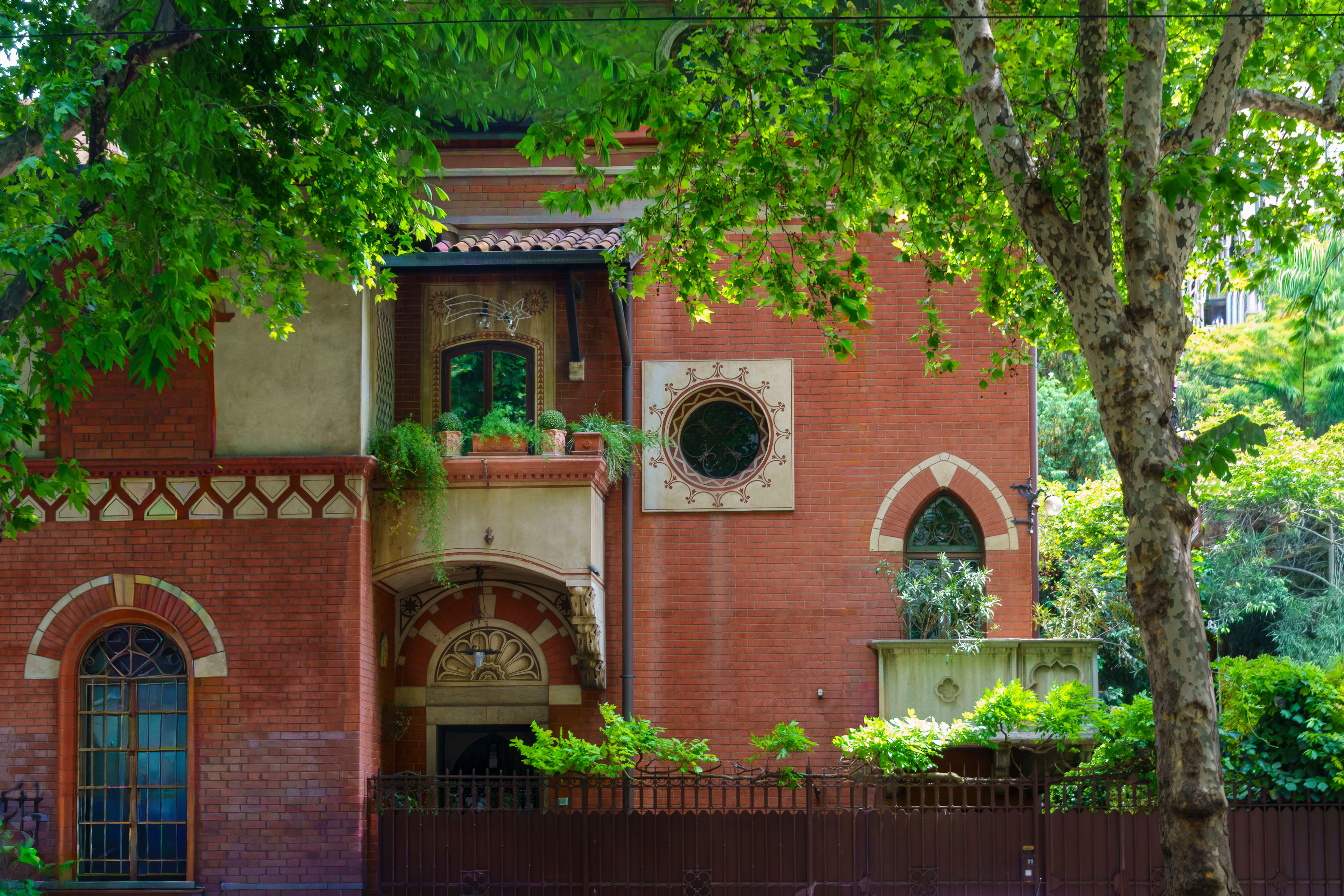 A beautiful red brick villa surrounded by lush greenery and architectural details.