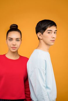 一幅充满活力的橙色背景肖像中，一位年轻男子和一位年轻女子并肩而立，展现了多样性