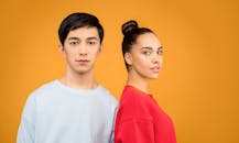 一对年轻夫妇自信地穿着休闲服，站在充满活力的橙色背景前