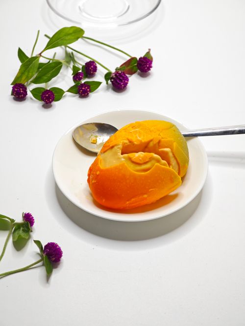 Free A vibrant mango slice served with a spoon on a white plate, decorated with purple globe amaranth flowers. Stock Photo