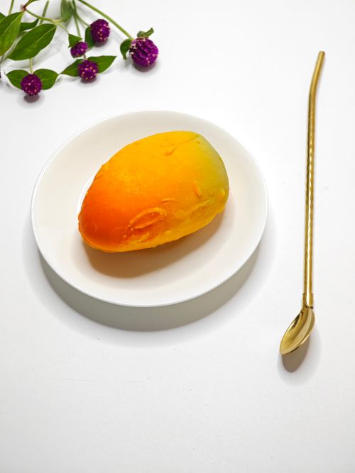 Free A ripe mango elegantly presented on a white plate with a golden spoon. Minimalist style. Stock Photo