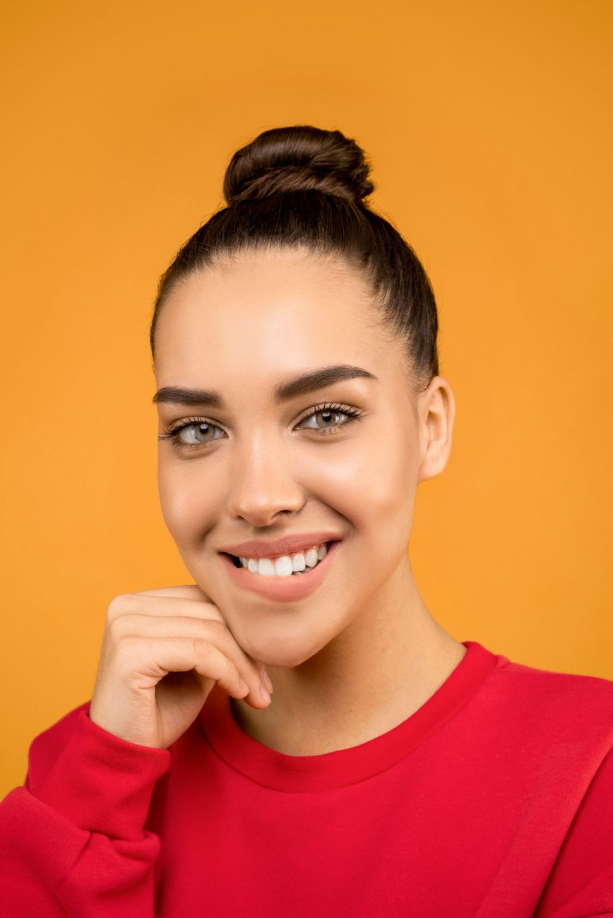 Portrait of a smiling young woman with an elegant hairstyle against a bright orange background.