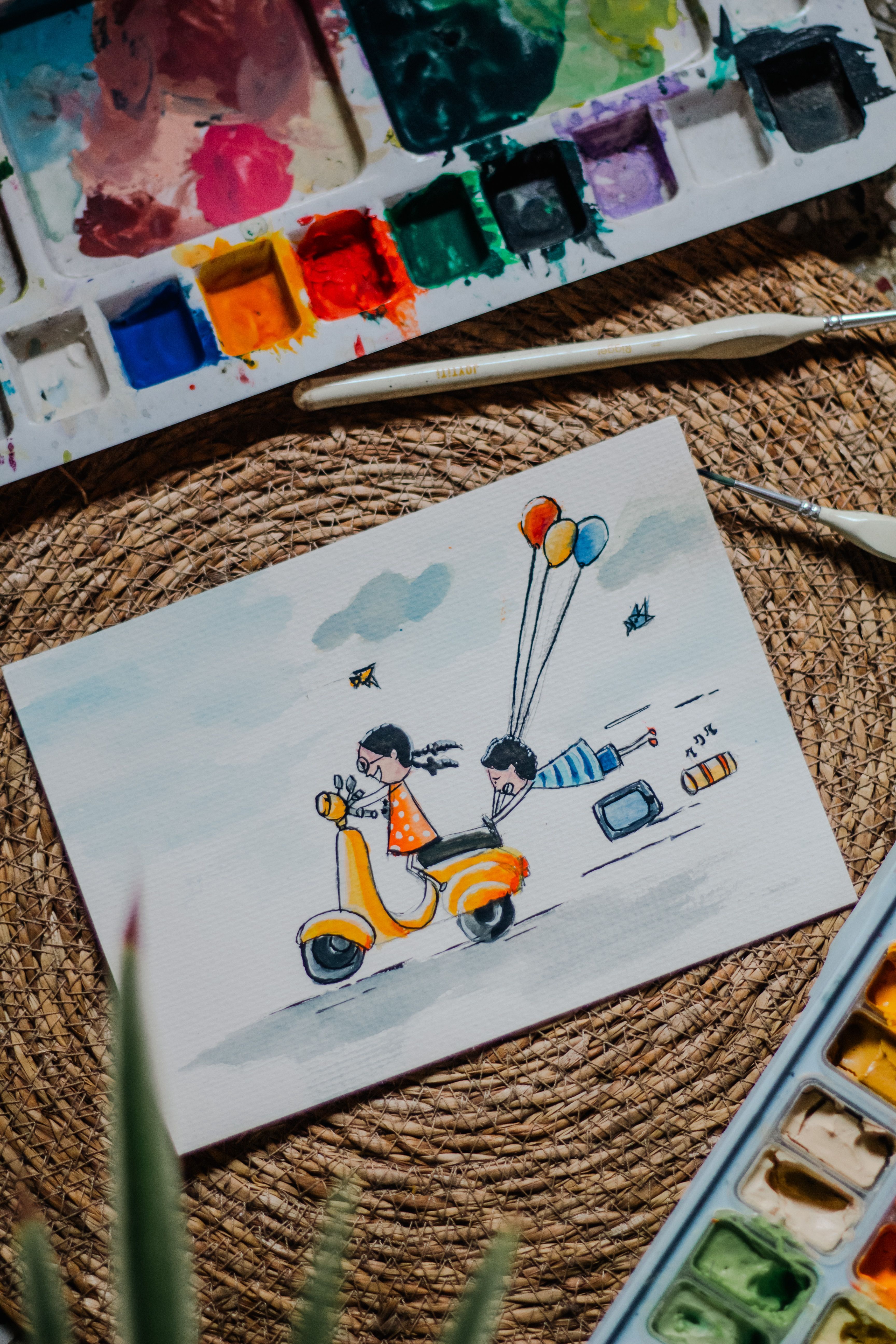 Artistic watercolor painting of children riding a scooter, surrounded by balloons and paint colors.