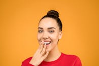 一位微笑的女人的肖像，手捂住嘴，背景是鲜艳的橙色