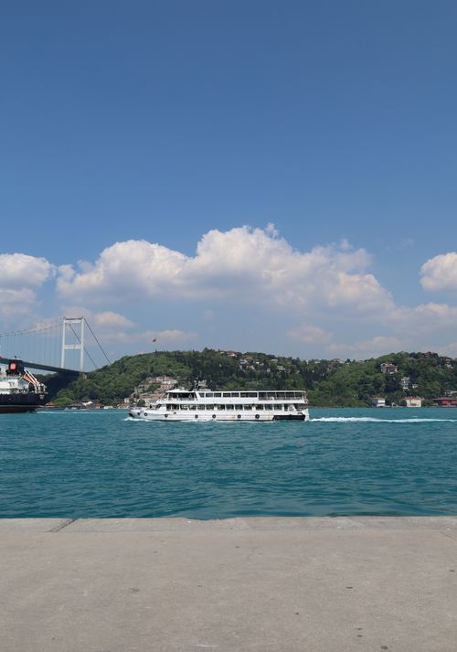 Free A ferry navigating the vibrant waters of the Bosphorus near the iconic Bosphorus Bridge under clear skies. Stock Photo