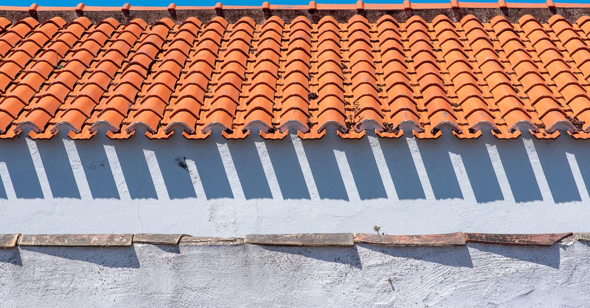 Close-up of a classic orange tiled roof casting shadows against a clear blue sky.