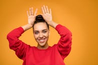 充满活力的肖像，一位年轻女子穿着红色毛衣在黄色背景上顽皮地摆姿势