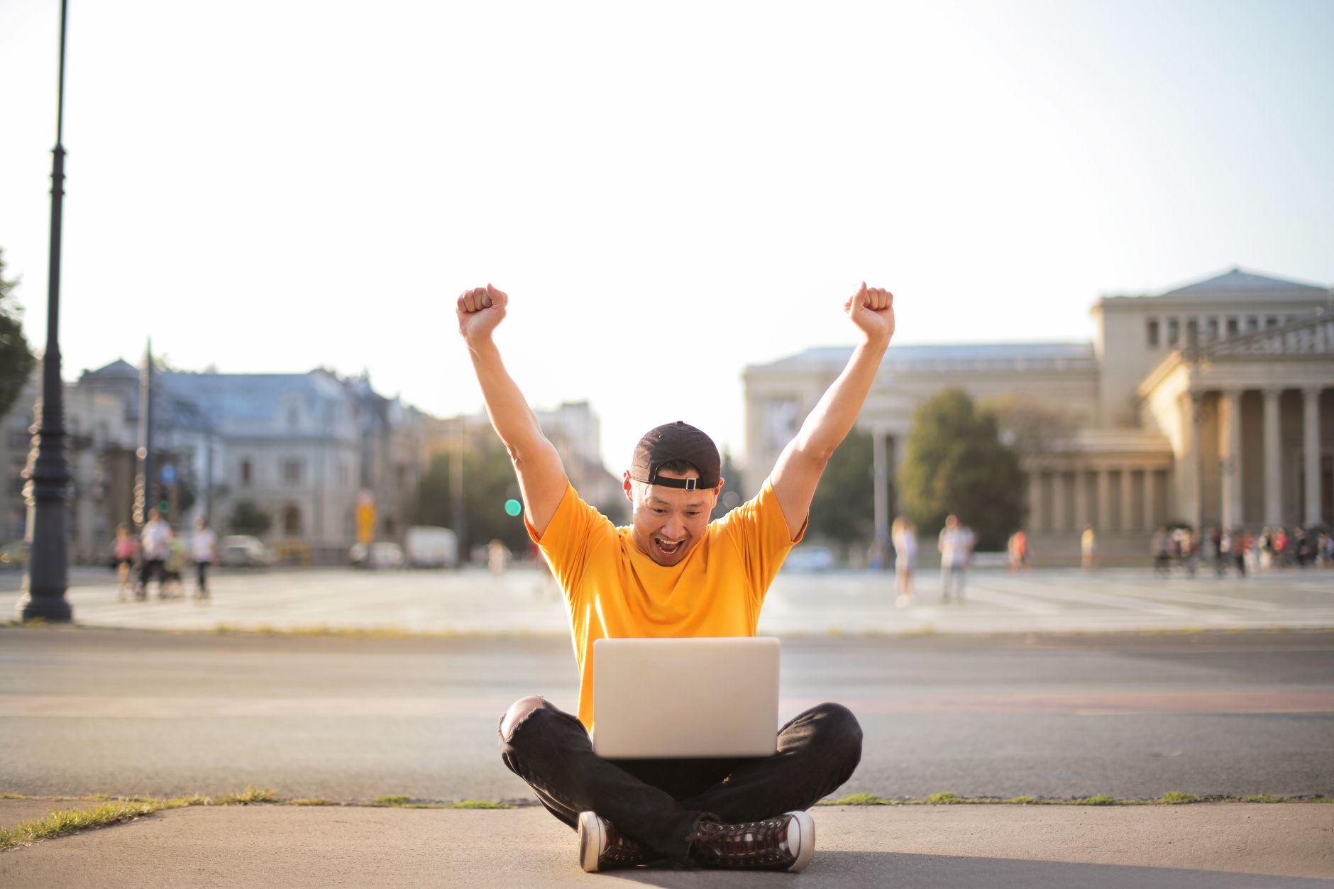 零粉絲網路賺錢三步驟:平台內容產品變現順序 Excited young man in yellow shirt cheers while sitting outdoors with a laptop.