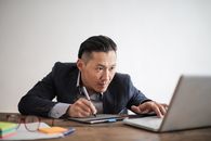 亚洲人紧张地坐在办公桌前，专注地使用笔记本电脑工作，展现了他们的注意力和技术运用
