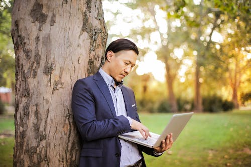 Man wearing Navy Blue Blazer Leaning on Tree Using Laptop 