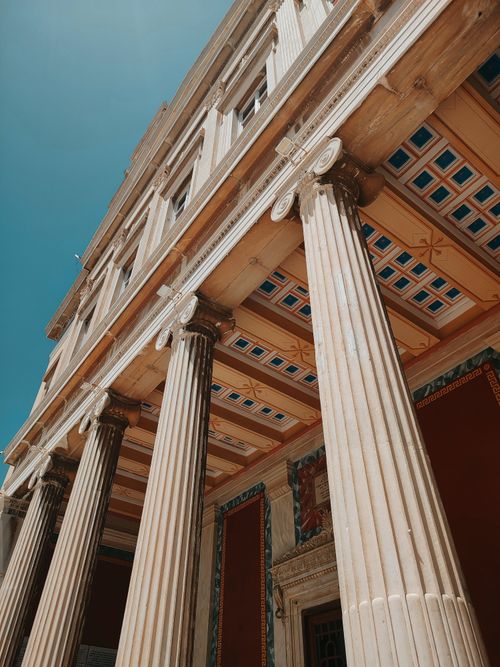Free A low-angle view of architectural columns with detailed carvings and a clear blue sky. Stock Photo