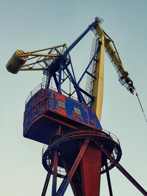 Free A colorful, industrial crane stands tall against a clear blue sky, showcasing engineering and construction themes. Stock Photo