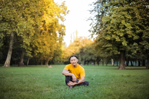 Yeşil çim Sahada Tek Başına Oturan Turuncu Tişörtlü Adam Akıllı Telefonunu Tutarken Fotoğrafı