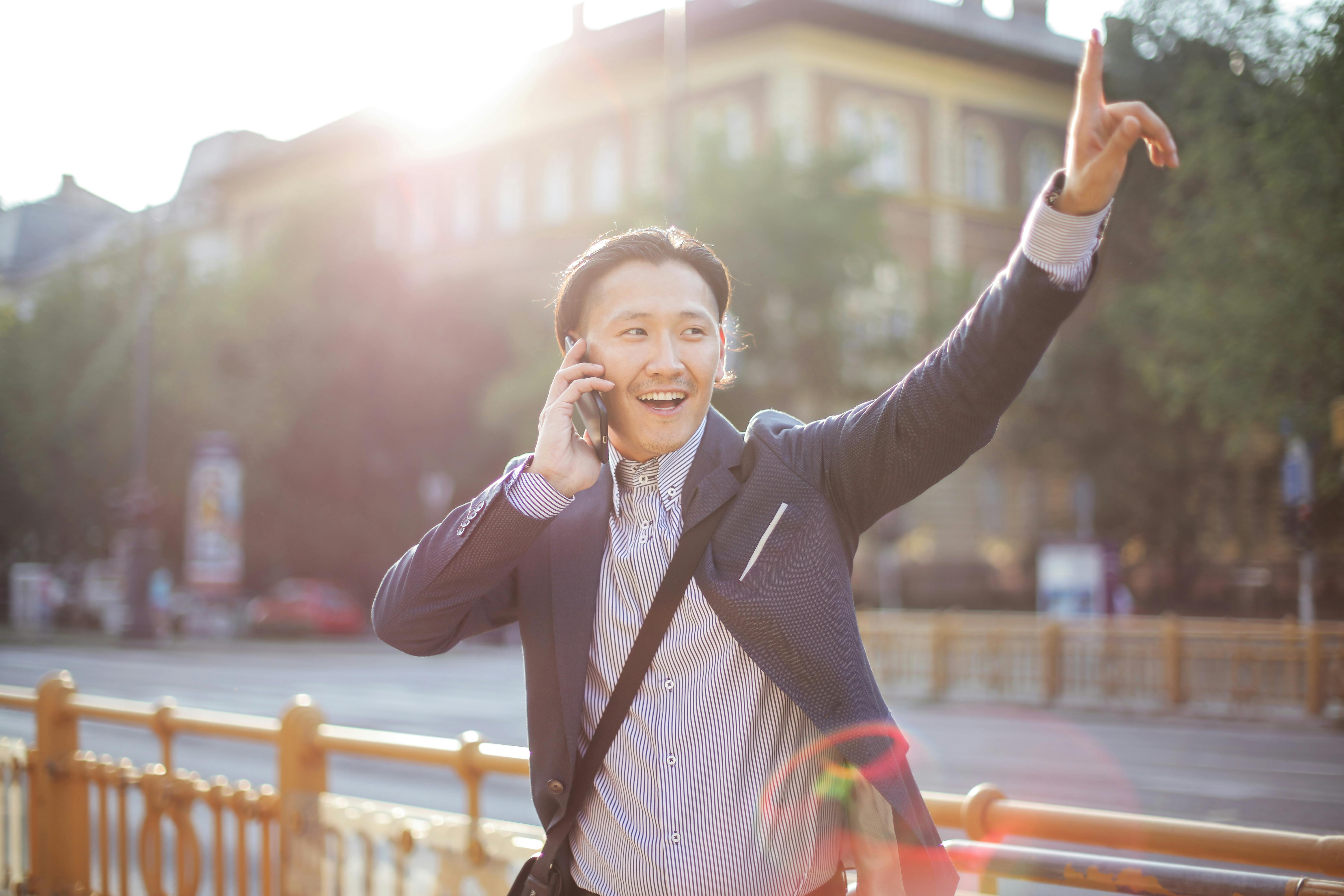 cheerful asian businessman chatting on phone and hailing cab