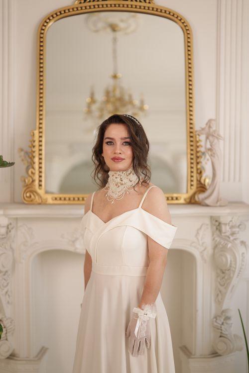 Free A beautiful bride stands by a classic ornate mirror, exuding timeless elegance in an off-shoulder vintage dress. Stock Photo