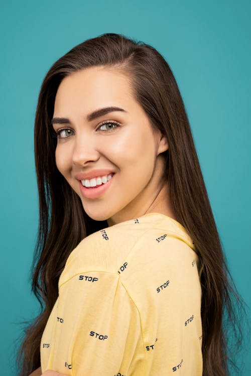 Free Portrait Photo of Smiling Woman in Yellow Top Posing In Front of Blue Background Stock Photo