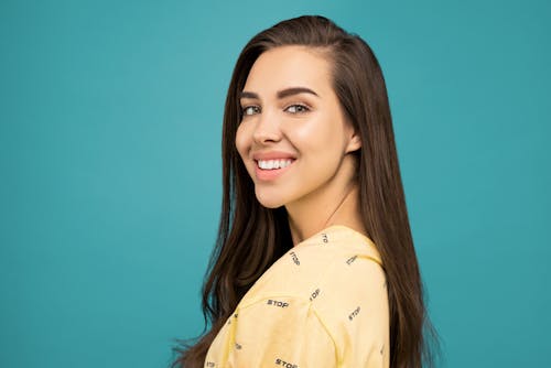 Free  Portrait Photo of Smiling Woman in Yellow Top Posing In Front of Blue Background Stock Photo