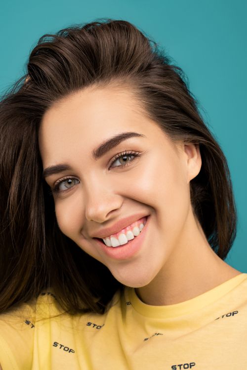 Free Charming portrait of a young woman with a joyful smile against a blue backdrop. Stock Photo