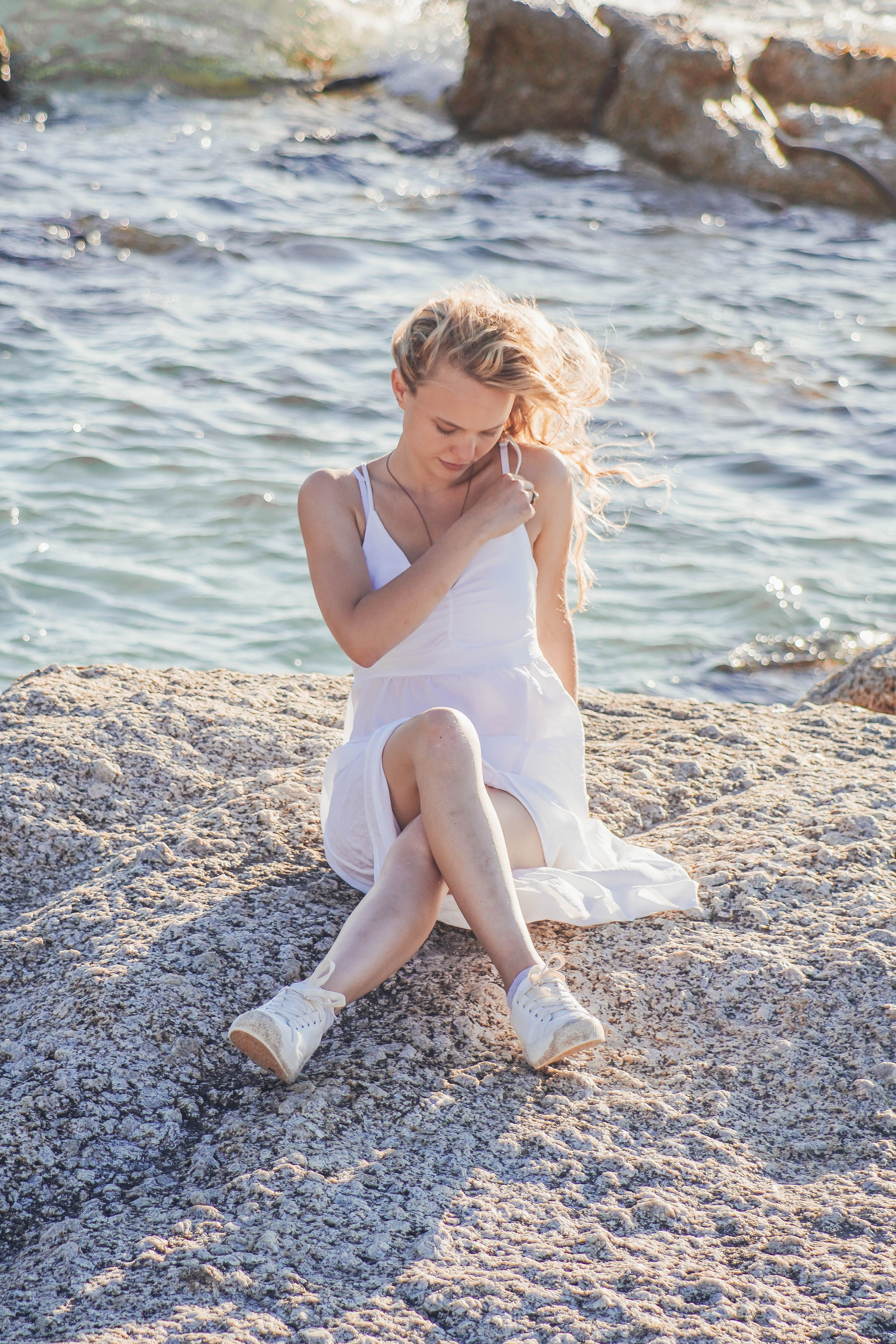 Woman in White Dress Sitting on Beach Rocks · Free Stock Photo