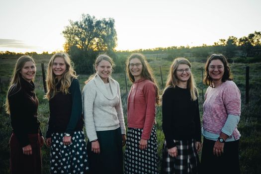 Six women stand together outdoors, smiling at sunset on a scenic field.