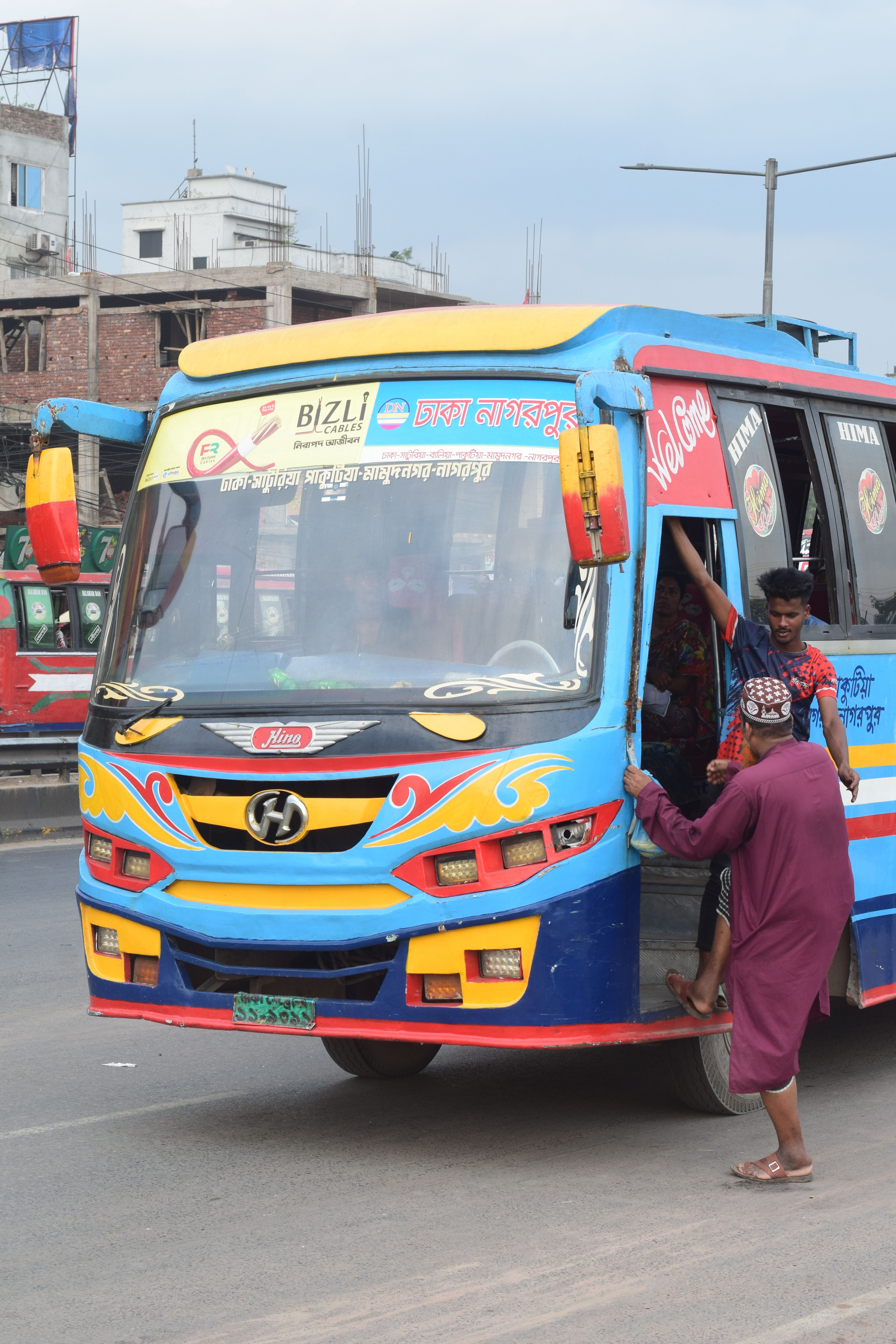 Vibrant local bus in Dhaka with passengers boarding on a busy street.