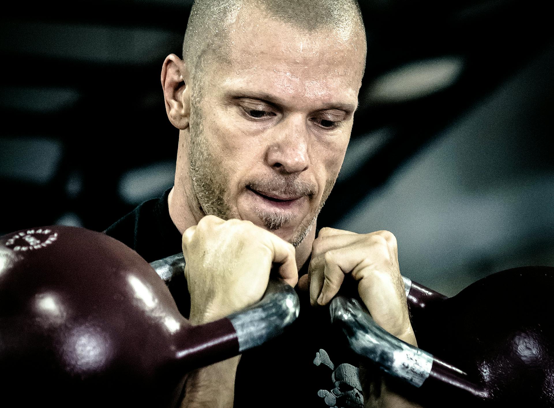 Focused man lifting kettlebells during an intense crossfit workout indoors.