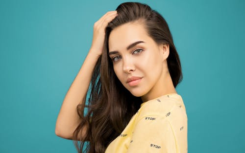 Close-up Portrait Photo of Woman in Yellow Top Posing In Front of Blue Background