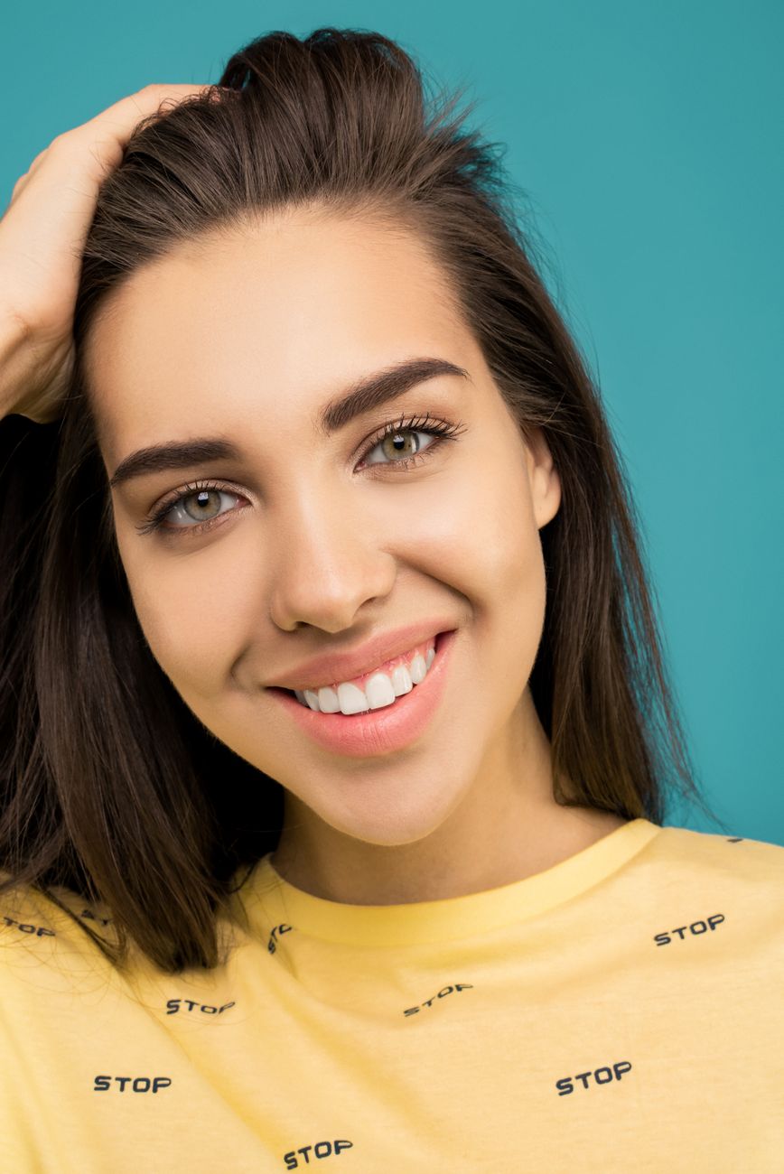 Portrait of a smiling young woman in a casual yellow shirt against a blue background.