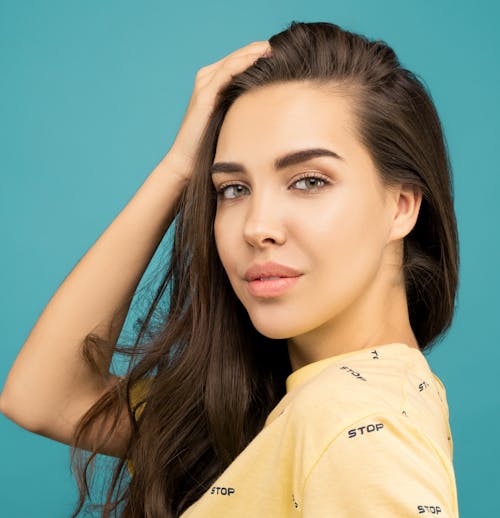 Close-up Portrait Photo of Woman in Yellow Top Posing In Front of Blue Background