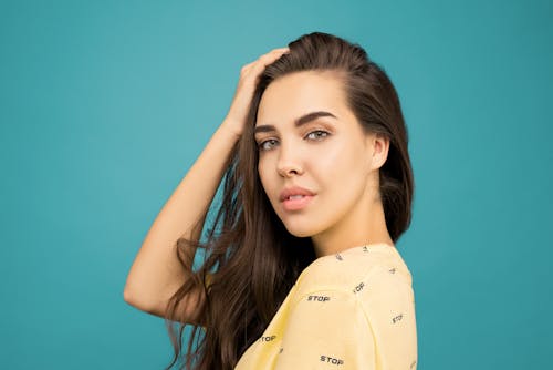 Close-up Portrait Photo of Woman in Yellow Top Posing In Front of Blue Background