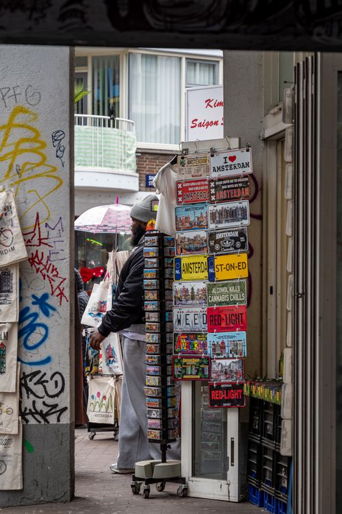 Free A vibrant street market selling Amsterdam-themed souvenirs, with graffiti and a partially visible shopper. Stock Photo