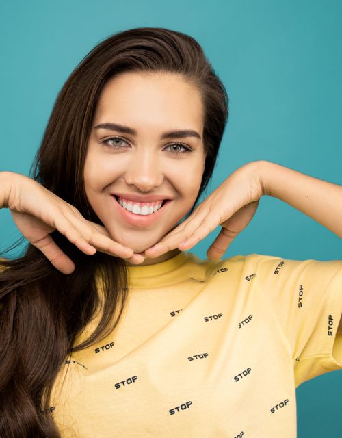 Free Cheerful woman posing with hands framing her face against a blue background. Stock Photo