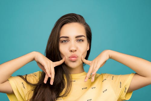 Free Portrait Photo of Woman in Yellow T-shirt Posing with Her Fingers on Her Cheeks Stock Photo