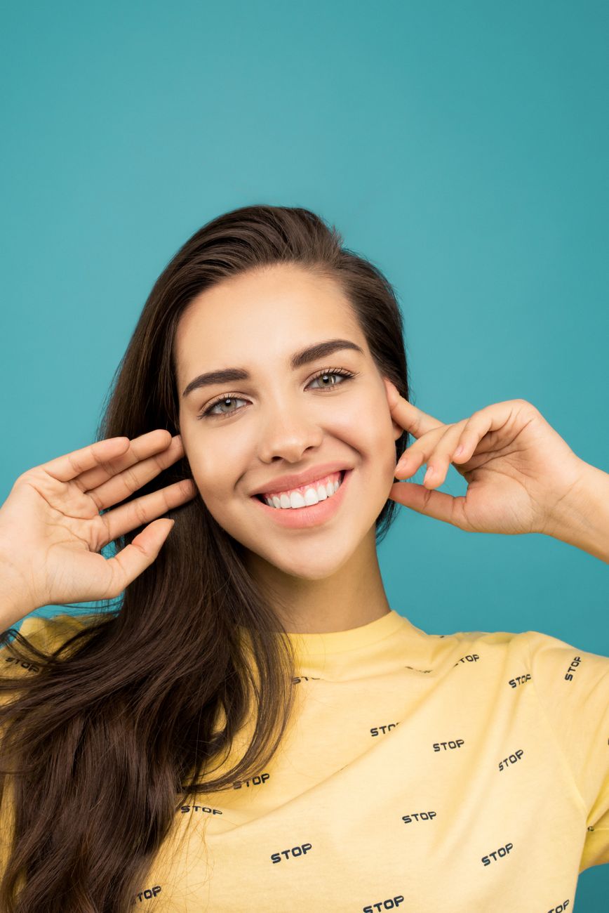 Portrait of a smiling woman with long hair wearing a yellow shirt against a turquoise background.