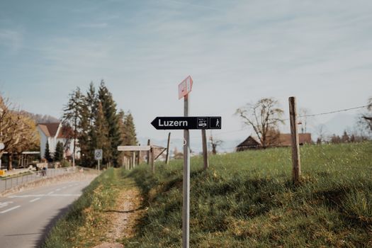 A scenic road sign pointing to Lucerne on a tranquil rural road in Switzerland.