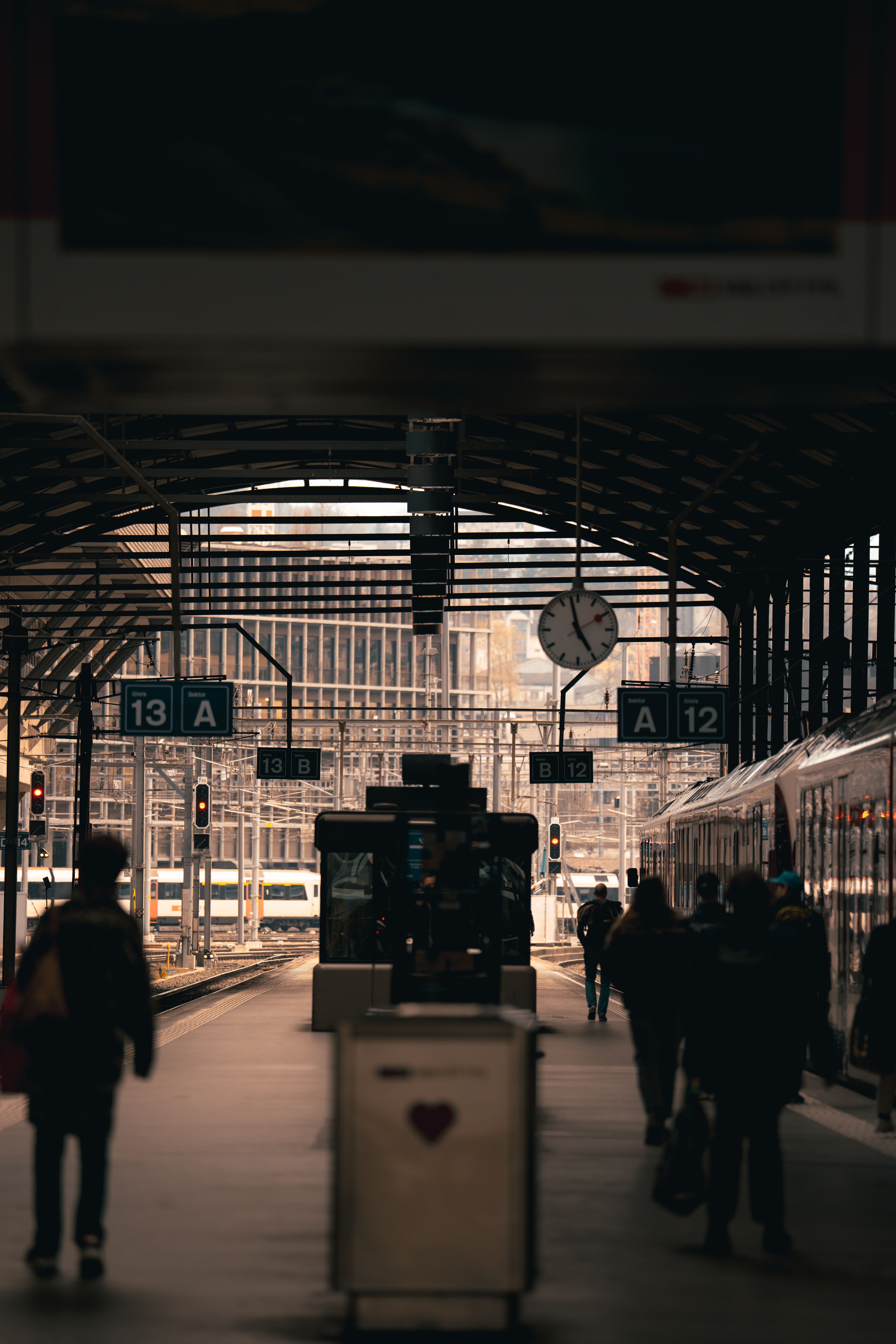 Travelers at Lucerne train station during early morning, with trains and iconic clock.