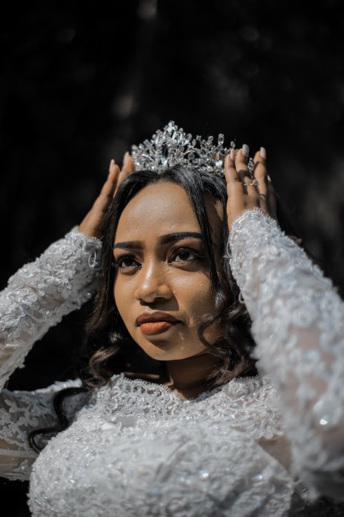 Free Thoughtful young ethnic bride in elegant white dress fixing crown and looking away during wedding celebration Stock Photo