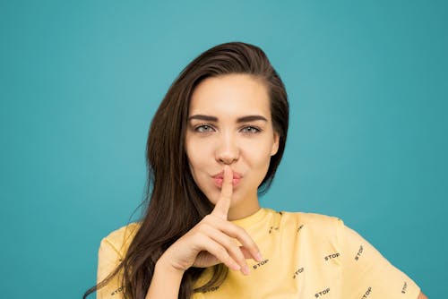 Porträtfoto Der Frau Im Gelben T Shirt, Das Das Shh Zeichen Tut, Während Es Vor Blauem Hintergrund Steht