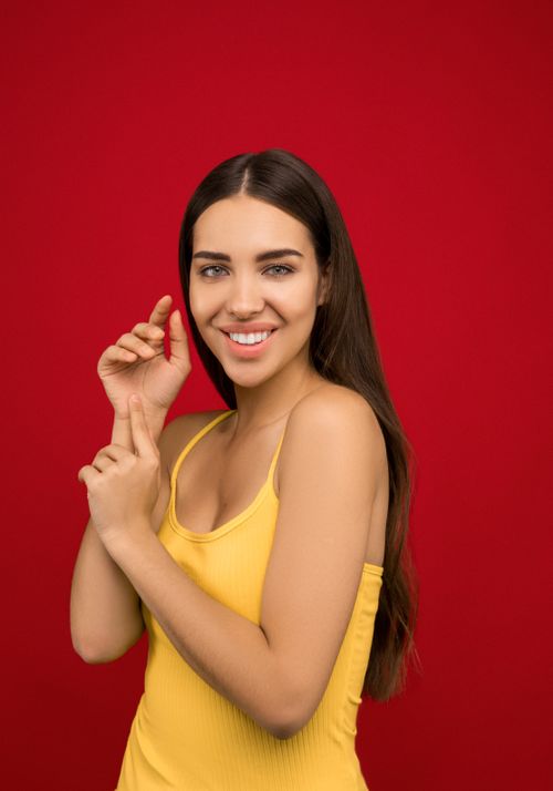 Free Portrait of a young, smiling woman in a yellow tank top against a red background. Stock Photo
