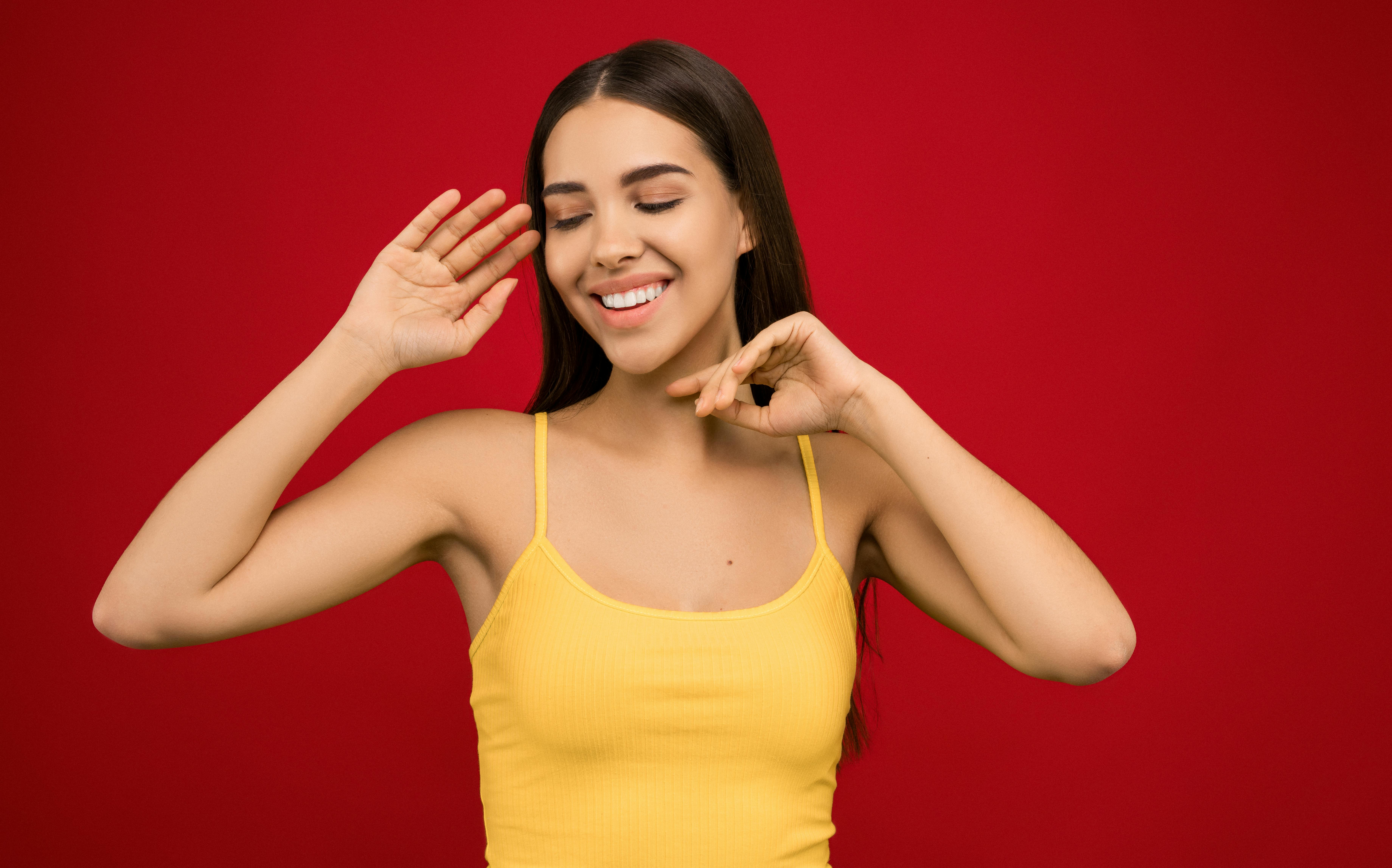 一位开朗的女人穿着黄色背心，在充满活力的红色背景下嬉戏地摆着姿势