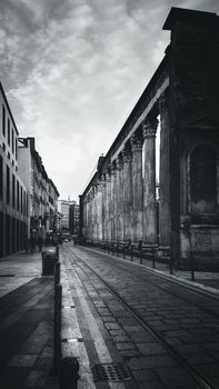Black and white photo of ancient Roman columns on a Milan street, Italy, showcasing historical architecture.