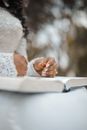 Low angle of crop unrecognizable bride in white dress sitting with book on knees and holding golden ring during wedding ceremony in garden